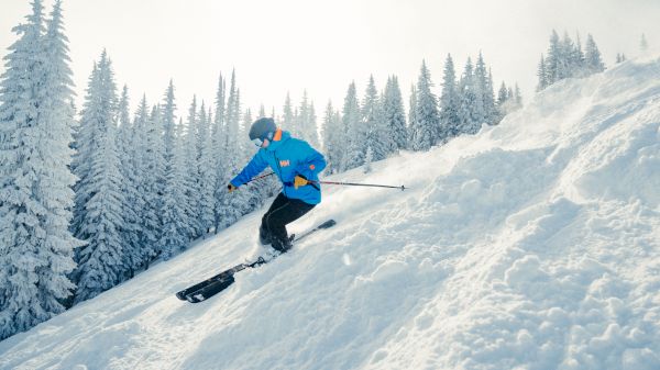 A skier in a blue jacket and helmet is skiing downhill on a snowy slope surrounded by snow-covered trees.