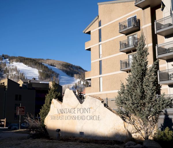 The image shows a building complex with a sign reading "Vantage Point 508 East Lionshead Circle" and a mountain with snow in the background.