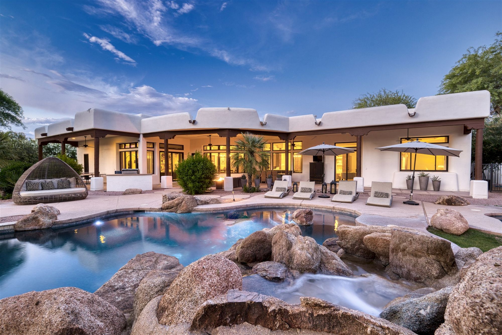 A modern house with large windows, surrounded by a landscaped yard; features a swimming pool with rocks and outdoor seating area.