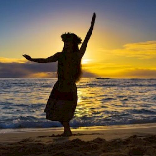 A person performs a hula dance on the beach at sunset, silhouetted against the sea and colorful sky.
