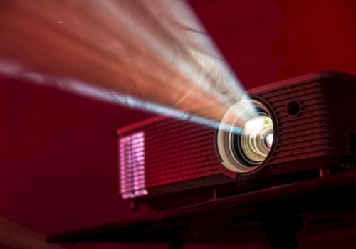 A projector is lit, casting a beam of light across a dim, red-lit room.