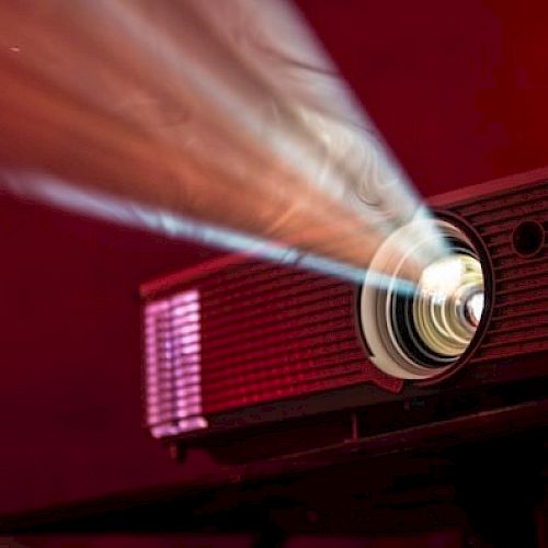 A projector is lit, casting a beam of light across a dim, red-lit room.