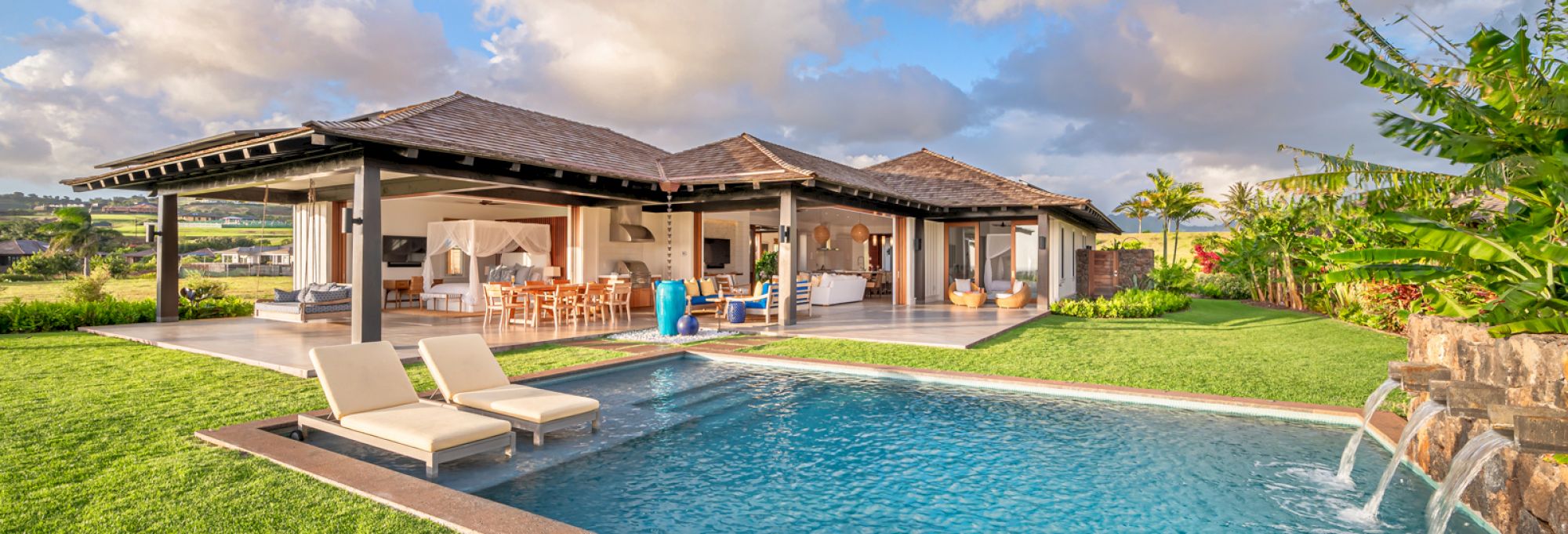 A luxurious open-concept home featuring poolside lounge chairs, lush green lawn, and modern architectural design with outdoor seating and dining areas.