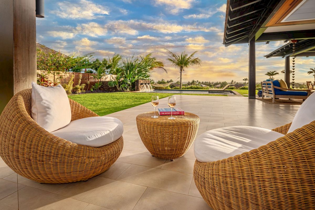 Outdoor patio with rattan chairs, small table, glasses of wine, and a scenic view of a garden and sky.