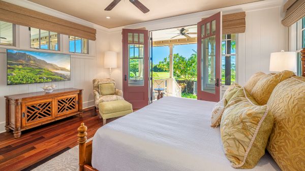 The image shows a cozy bedroom with a bed, armchair, wooden furniture, and an open door leading to a scenic outdoor view.