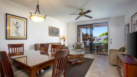 A modern living room with a dining area, ceiling fan, and patio doors leading outside, featuring artwork and a flat-screen TV.