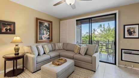 A cozy living room with a sectional sofa, artwork, lamp, and sliding glass doors leading to a balcony with a view.
