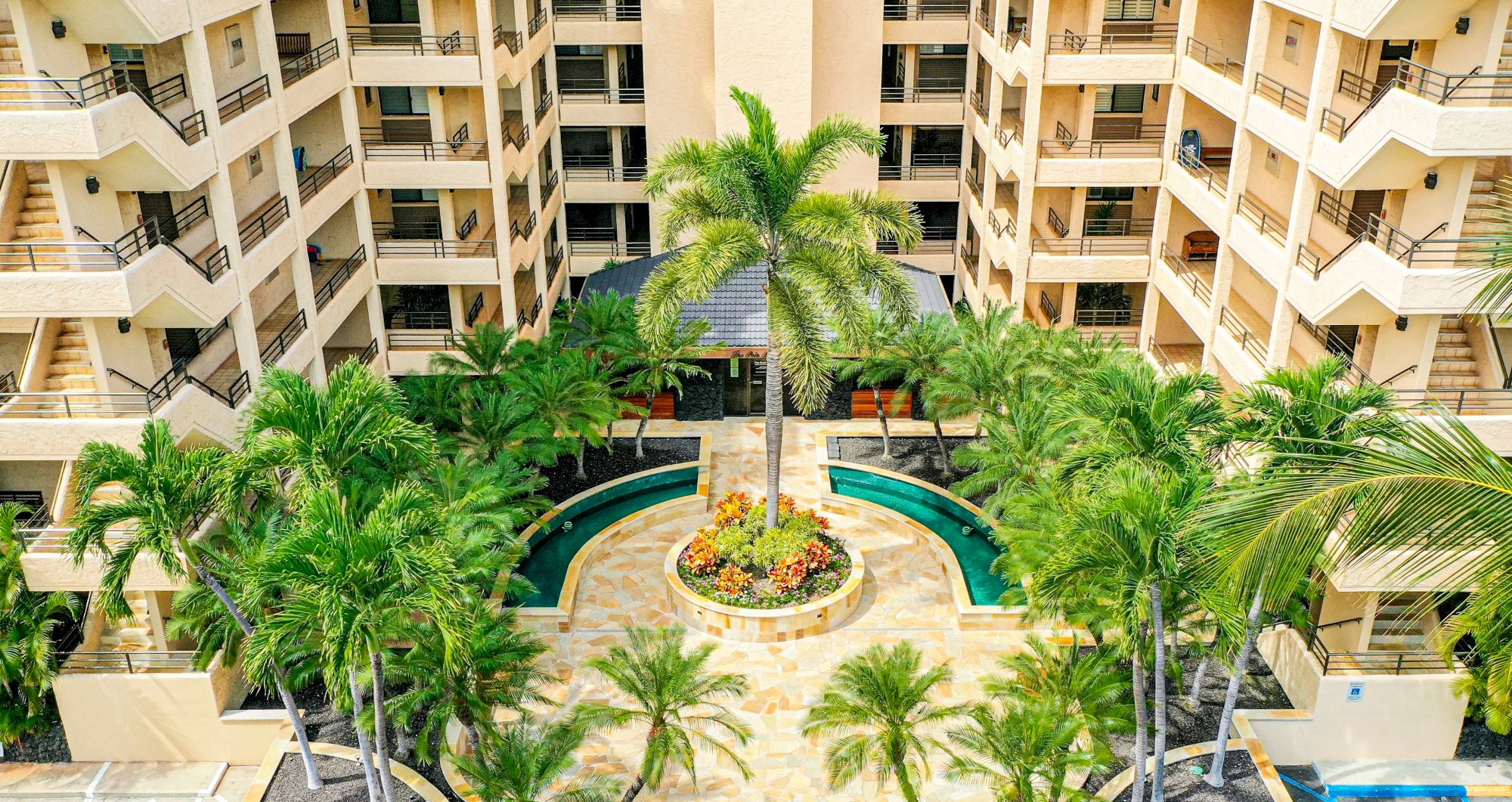The image shows a courtyard of a building with multiple floors, featuring a central landscaped area with palm trees and surrounding balconies.