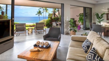 A luxurious living room opens to a beachfront view, with modern furniture, tropical plants, and stylish decor creating a serene atmosphere.