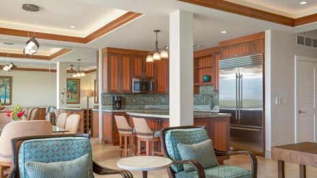 A modern, open-concept living space with a kitchen, island seating, and a cozy sitting area. Natural wood and teal accents are featured.