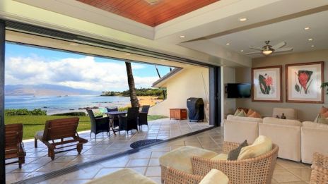 Open living room with comfortable seating, artwork, and a view of a patio overlooking the ocean under a clear sky.