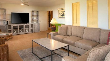 A cozy living room with a large beige sectional sofa, coffee table, TV, shelves, and artwork on the wall creating a relaxing space.