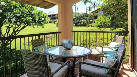 A patio with a glass table, four wicker chairs, lush greenery, and a scenic view.