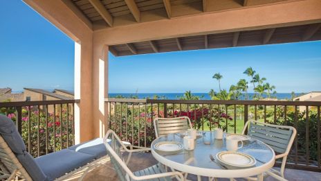 A patio with a table set for four offers a view of palm trees and the sea under a wooden roof.