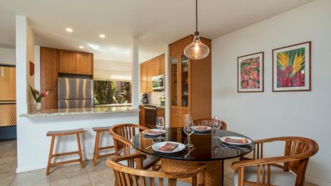 A cozy dining area with a round table, wooden chairs, and a modern kitchen in the background, accented by framed wall art.