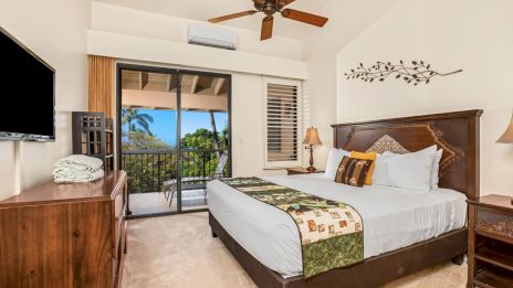 A bedroom features a large bed, a wall-mounted TV, a ceiling fan, and a balcony with a view of palm trees and a clear sky.