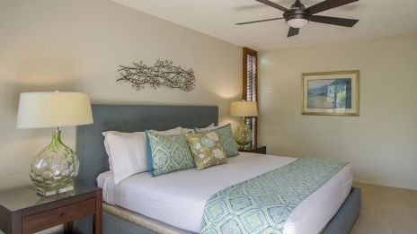 A cozy bedroom featuring a large bed, stylish lamps, a decorative metal wall art, and a ceiling fan, creating a relaxing atmosphere.