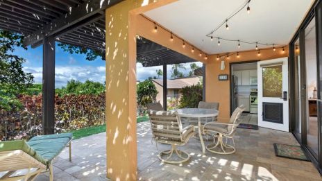 A cozy patio with a pergola, string lights, outdoor seating, and lush greenery, creating a welcoming and relaxing atmosphere.