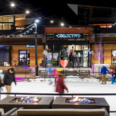 The image shows a lively night scene at a retail area with people skating, colorful lights, and a warm fire pit.