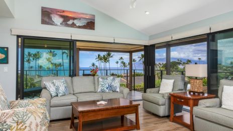 A cozy living room with ocean views, featuring gray sofas, a wooden coffee table, and large windows letting in ample natural light.