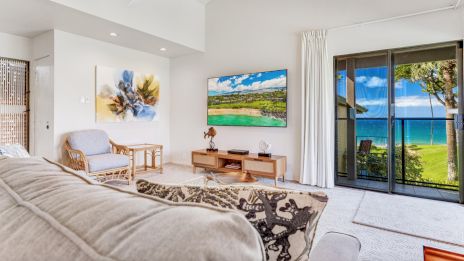 A cozy living room with a sofa, art, TV, and a view of the ocean through sliding glass doors.