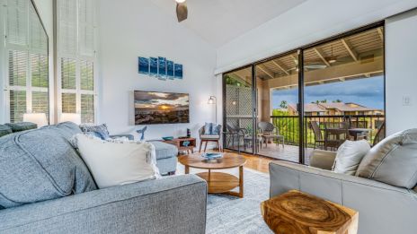 A modern living room with gray sofas, wooden accents, large sliding glass doors, and a view of a balcony overlooking greenery.