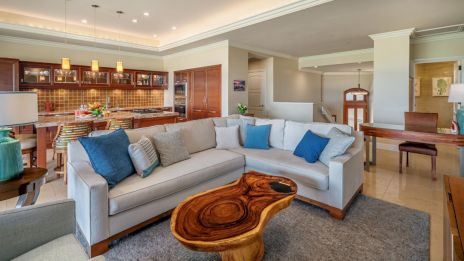 A modern living room with a white sectional sofa, wooden coffee table, a kitchen in the background, and contemporary decor throughout.