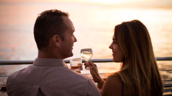 A couple enjoys drinks while sitting by the water during sunset, creating a romantic atmosphere.