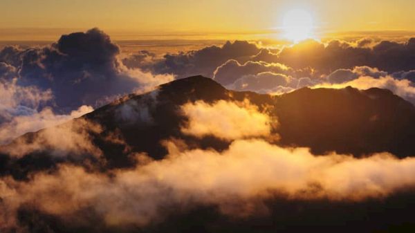 A stunning sunrise over a mountain peak with clouds illuminated in warm hues, creating a breathtaking and serene landscape scene.