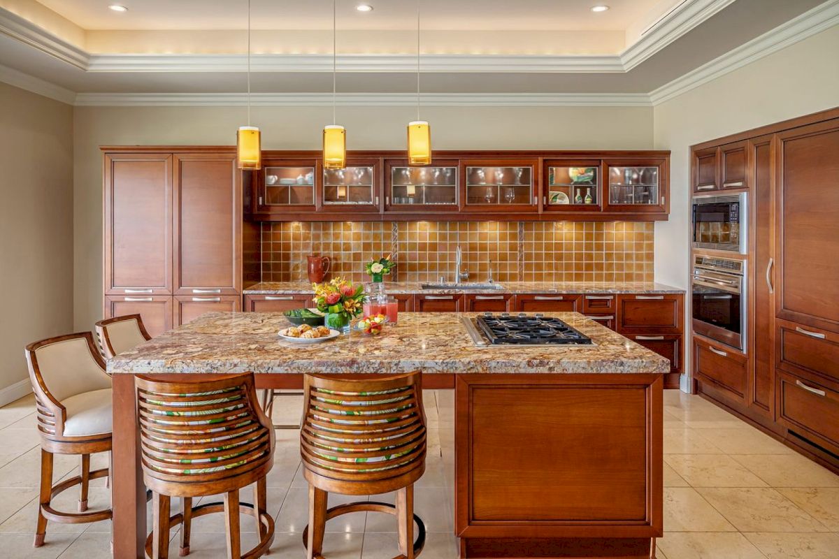 A modern kitchen with a granite island and three bar stools, wooden cabinets, pendant lights, and a tiled backsplash completes the look.