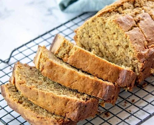 Banana bread slices cooling on a wire rack, golden crust, soft moist interior, fresh and homey.
