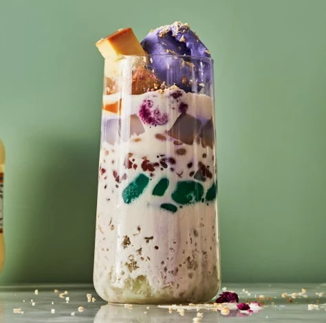 A tall, layered smoothie with purple top, green embellishments, and white yogurt or milk layers, finished with a gold-edged garnish.