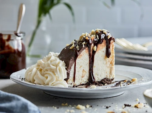 A slice of rich chocolate cake with vanilla ice cream and whipped cream on the side, drizzled with chocolate sauce and crumbs.