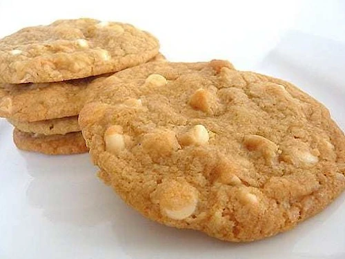 Fresh peanut butter cookies with chunky nuts, golden and crumbly, stacked on a white surface.