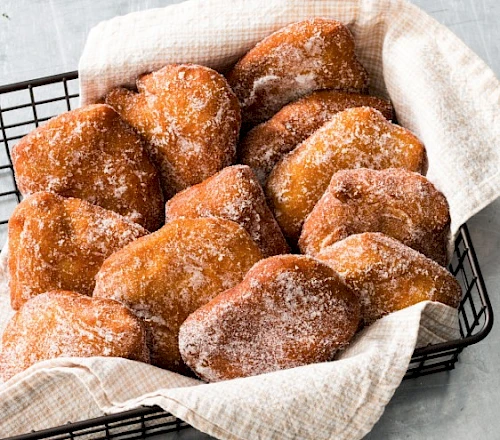 A basket of sugar-dusted churro-like fried pastries, warm and fluffy, nestled in a cloth-lined rack.
