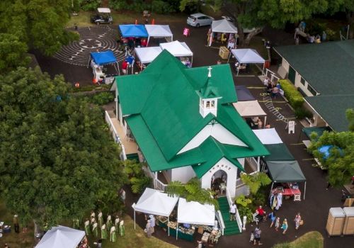 An aerial view of a green-roof church with tents and people around, likely at a market or outdoor event near trees and parked cars.