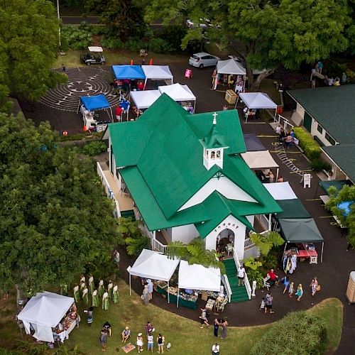 An aerial view of a green-roof church with tents and people around, likely at a market or outdoor event near trees and parked cars.