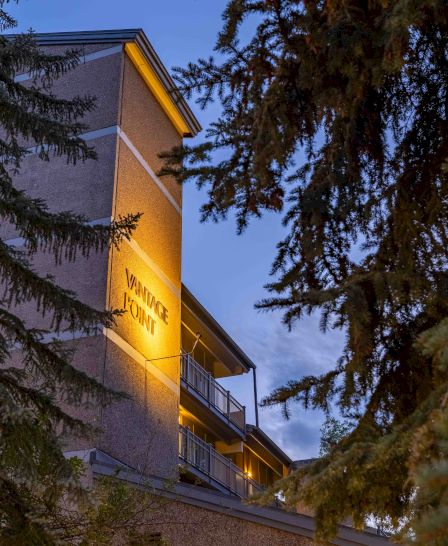 The image showcases a building partially visible through trees, illuminated at dusk, creating a serene and inviting atmosphere.