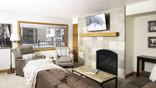 A modern living room with a cozy couch, flat-screen TV, warm colors, and a large window showing snowy scenery outside.