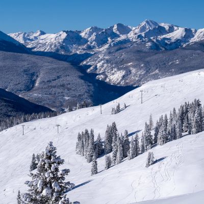 A stunning winter landscape featuring snow-covered mountains, pine trees, and ski lifts under a clear blue sky.