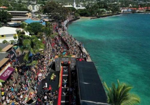 Aerial view of a coastal marathon event with crowds, a red finish line, and turquoise ocean on a sunny day.
