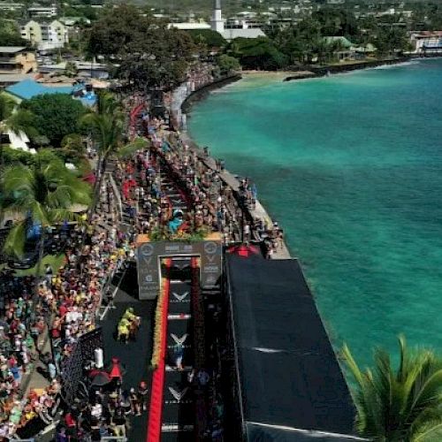 Aerial view of a coastal marathon event with crowds, a red finish line, and turquoise ocean on a sunny day.