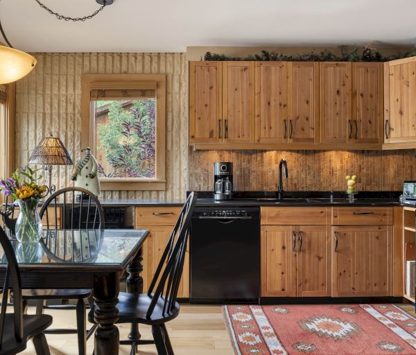A cozy kitchen with wooden cabinets, a black counter, a dining table, and a window view. Decorative elements add warmth and charm.