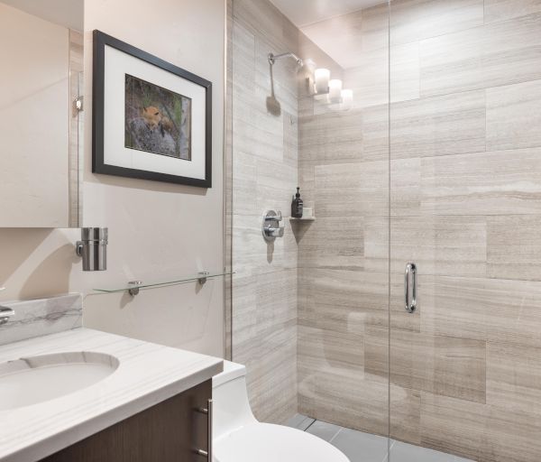 A modern bathroom with a glass shower, marble countertop sink, artwork on the wall, and neutral tiles throughout.