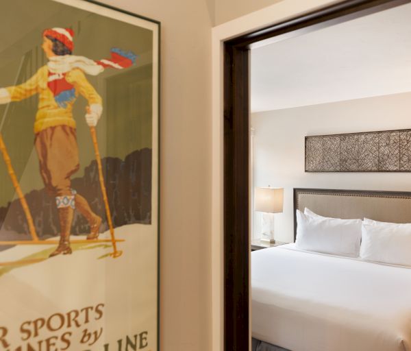 A cozy bedroom with a neatly made bed and a lamp, featuring a vintage winter sports poster on the wall.