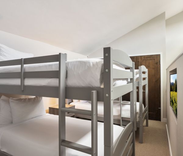 The image shows a room with two sets of gray bunk beds, white bedding, and a small window, creating a cozy sleeping space.