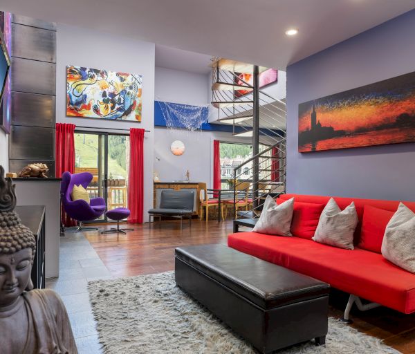 The image shows a modern living room with a red sofa, artwork on the walls, a spiral staircase, and a decorative Buddha statue.
