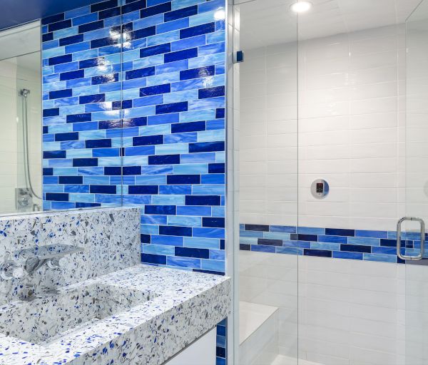 The image shows a modern bathroom with blue and white tiles, a speckled countertop, and a glass shower enclosure.