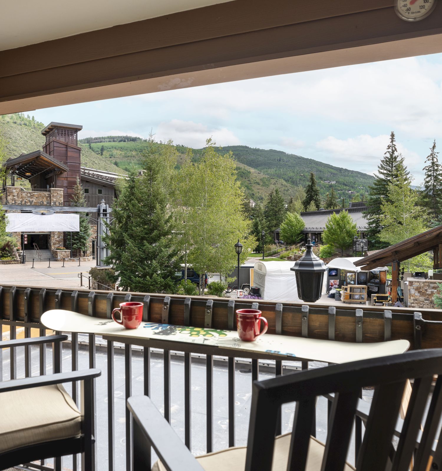 A balcony with chairs overlooking a scenic view of trees and a building in a mountainous area.