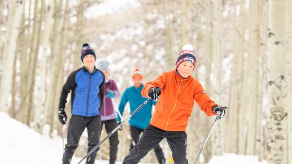 A group of people are cross-country skiing through a snowy forest, surrounded by tall trees.